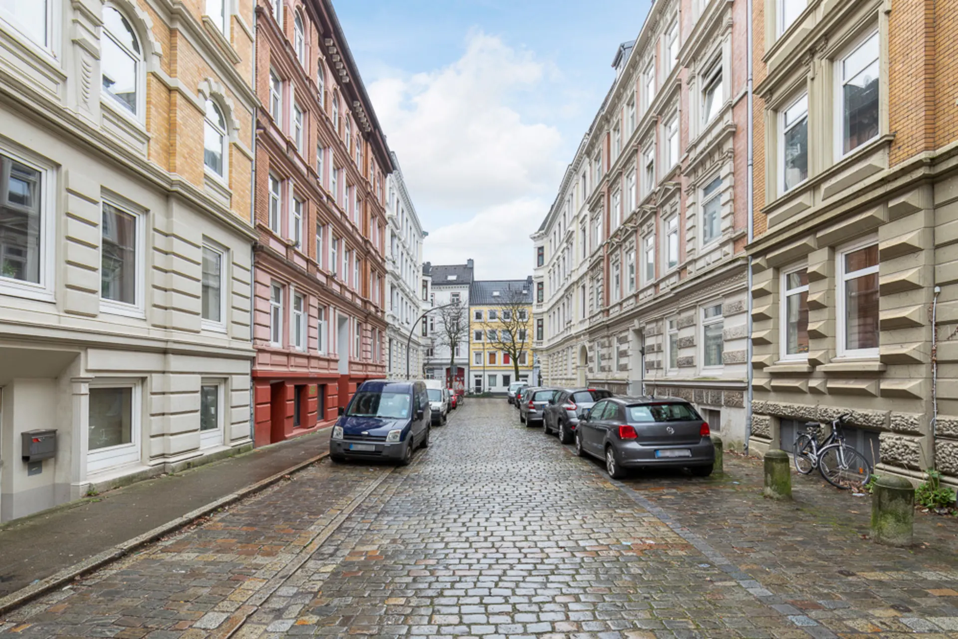 Pflastersteinstraße mit parkenden Autos und mehrstöckigen Wohnhäusern auf beiden Seiten.