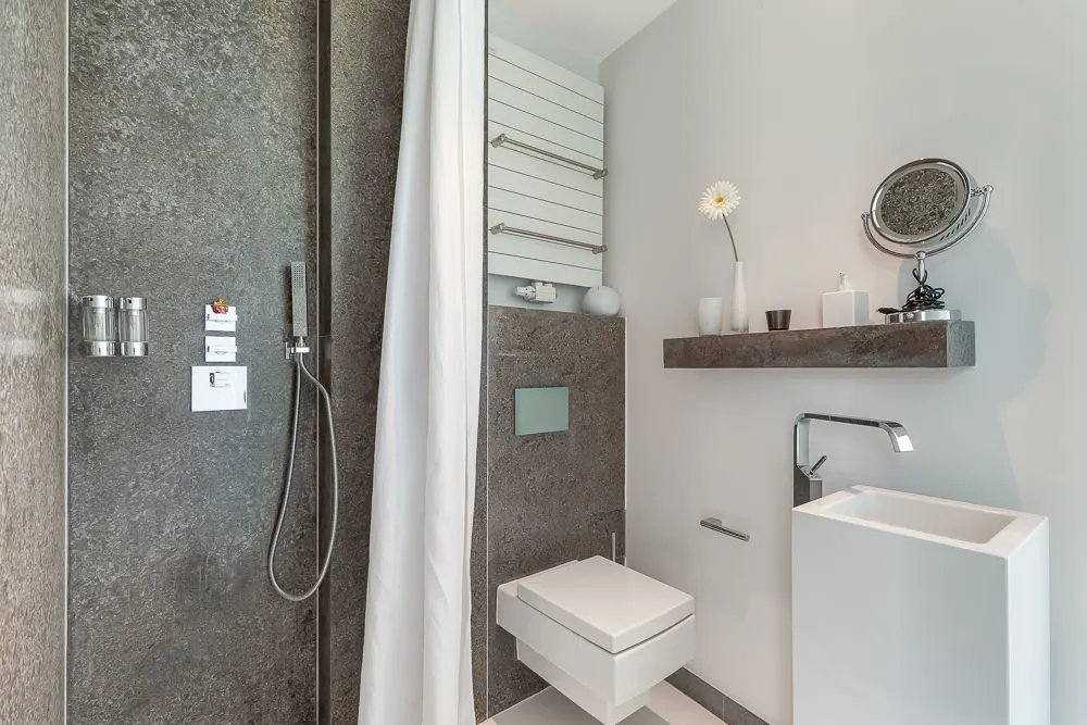 Modernes Badezimmer mit Dusche, WC, kleinem Waschbecken und Wandregal mit Dekoration.