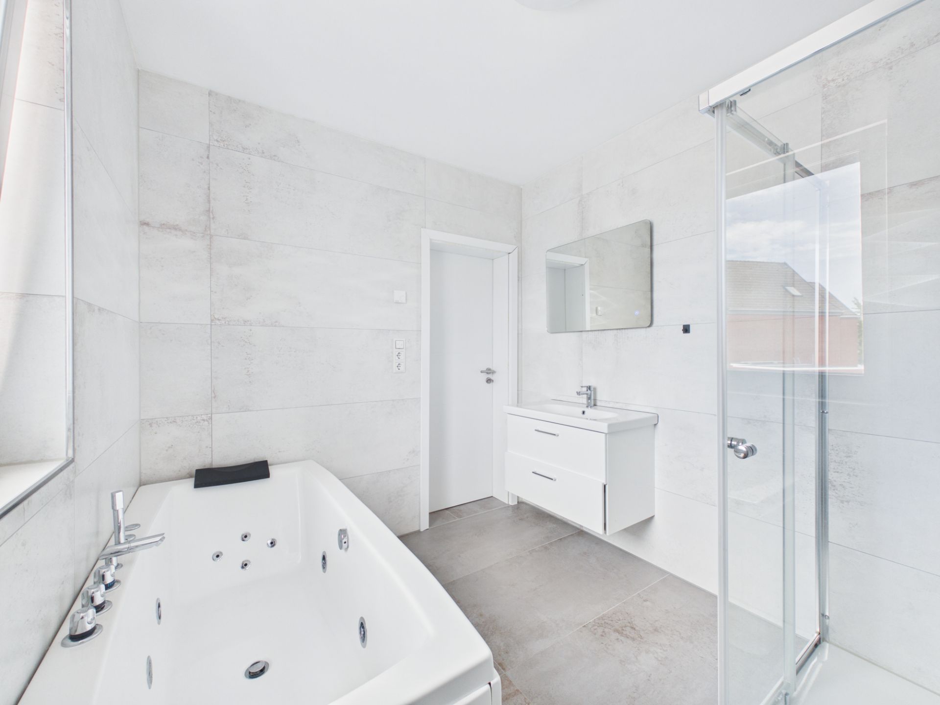 Modernes, weiß gefliestes Badezimmer mit Badewanne, Dusche und Waschbecken.