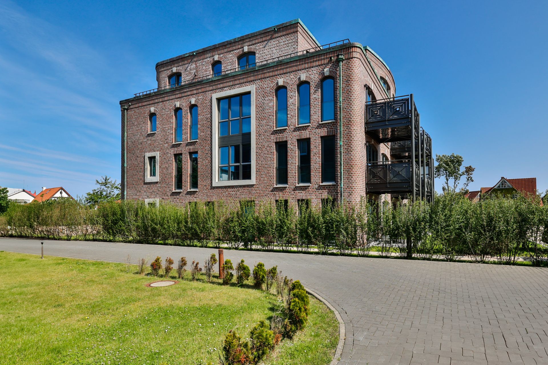 Modernes, mehrstöckiges Backsteingebäude mit großen Fenstern und Balkonen, umgeben von Grünanlage.