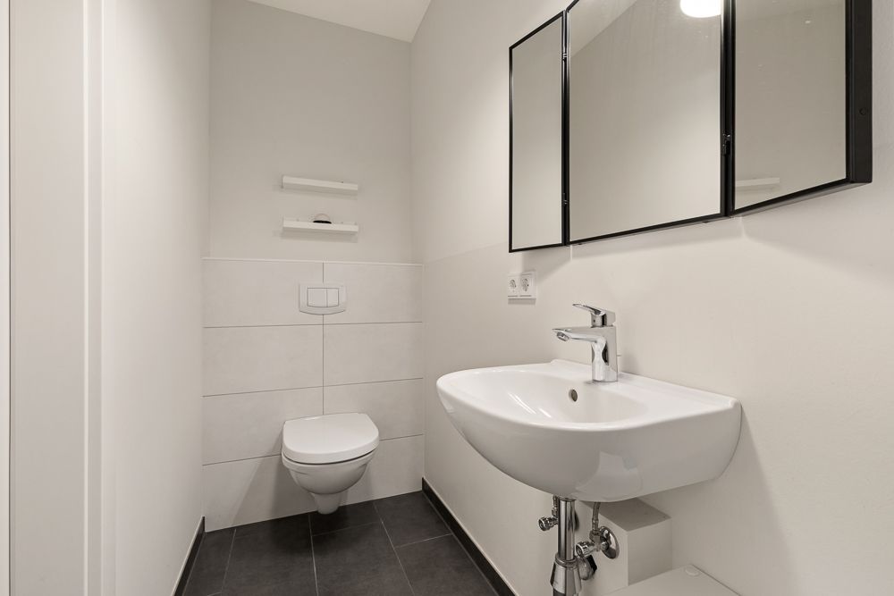 Modernes, weißes Badezimmer mit Wandtoilette, Waschbecken und Spiegelschrank.