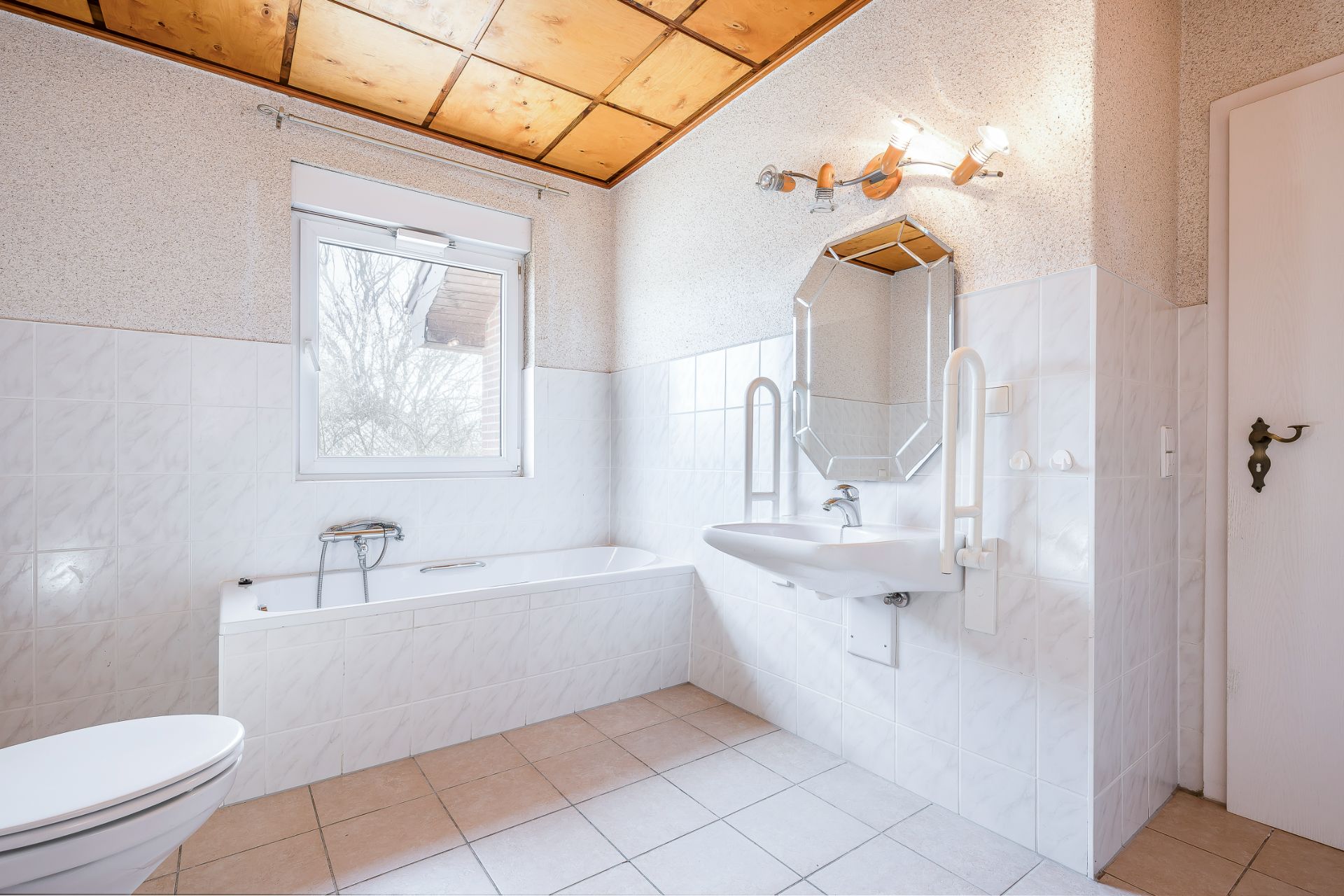 Helles Badezimmer mit Badewanne, Waschbecken, Spiegel und Fenster.