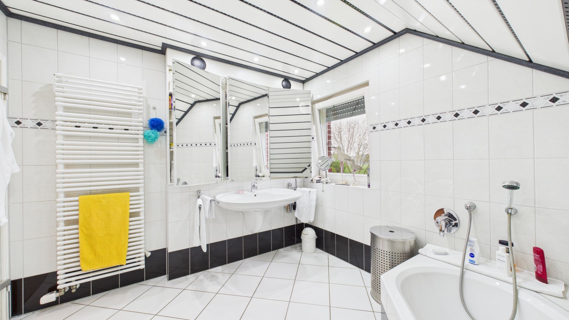Modernes Badezimmer mit Badewanne, großem Spiegel, Waschbecken und Fenster.