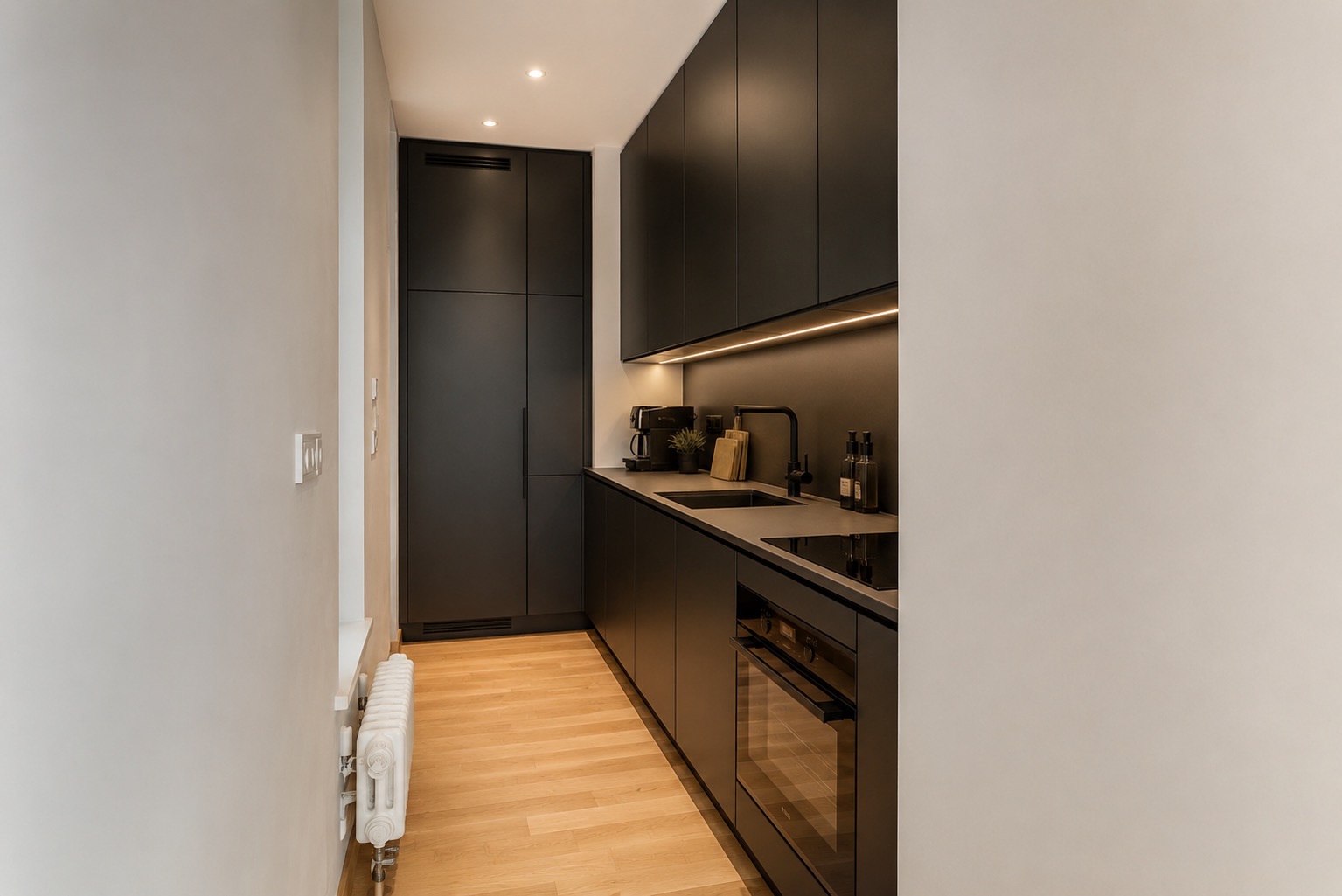 Schmale, moderne Küche mit schwarzen Schränken und Holzfußboden.