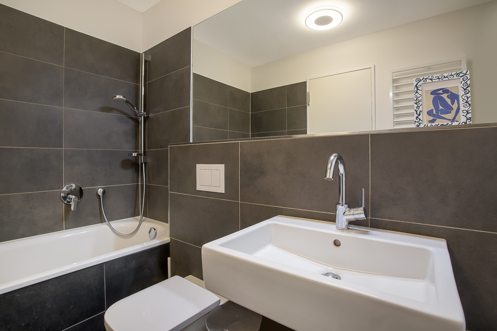 Modernes Badezimmer mit Badewanne, Dusche, Waschbecken und dunklen Wandfliesen.
