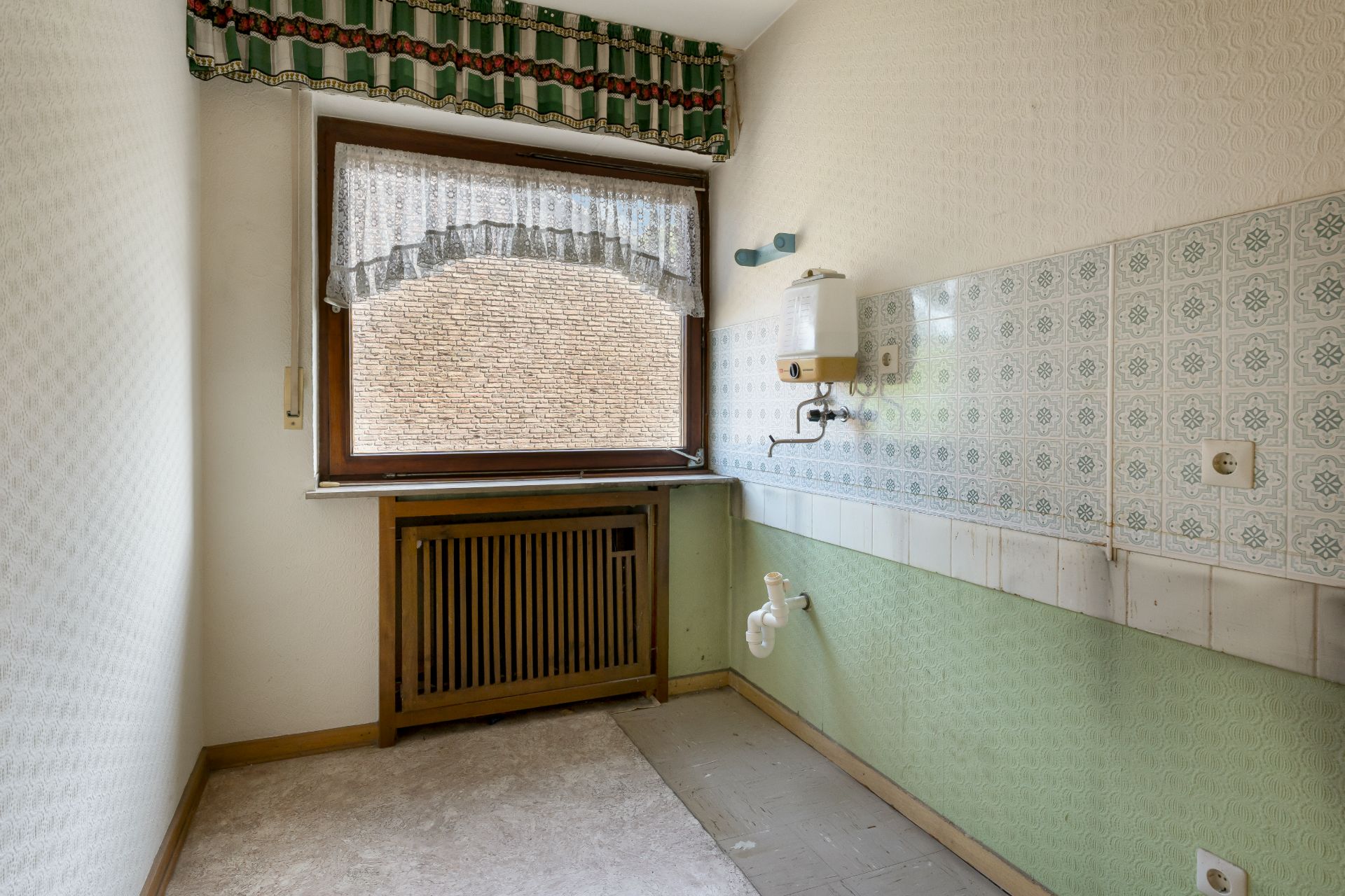 Kleiner leerer Raum mit Fenster, Heizung, gemusterten Fliesen und Wandarmatur.