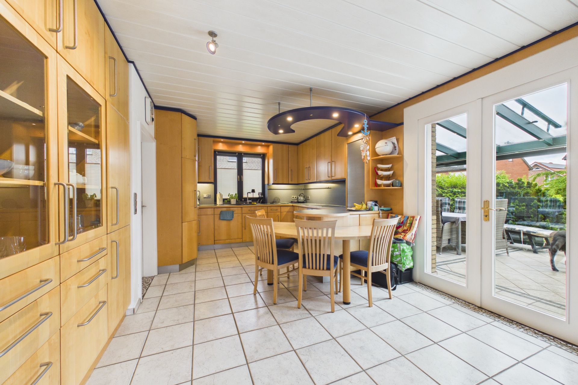 Helle Küche mit Holzmöbeln, Esstisch und Zugang zur Terrasse durch Glastüren.