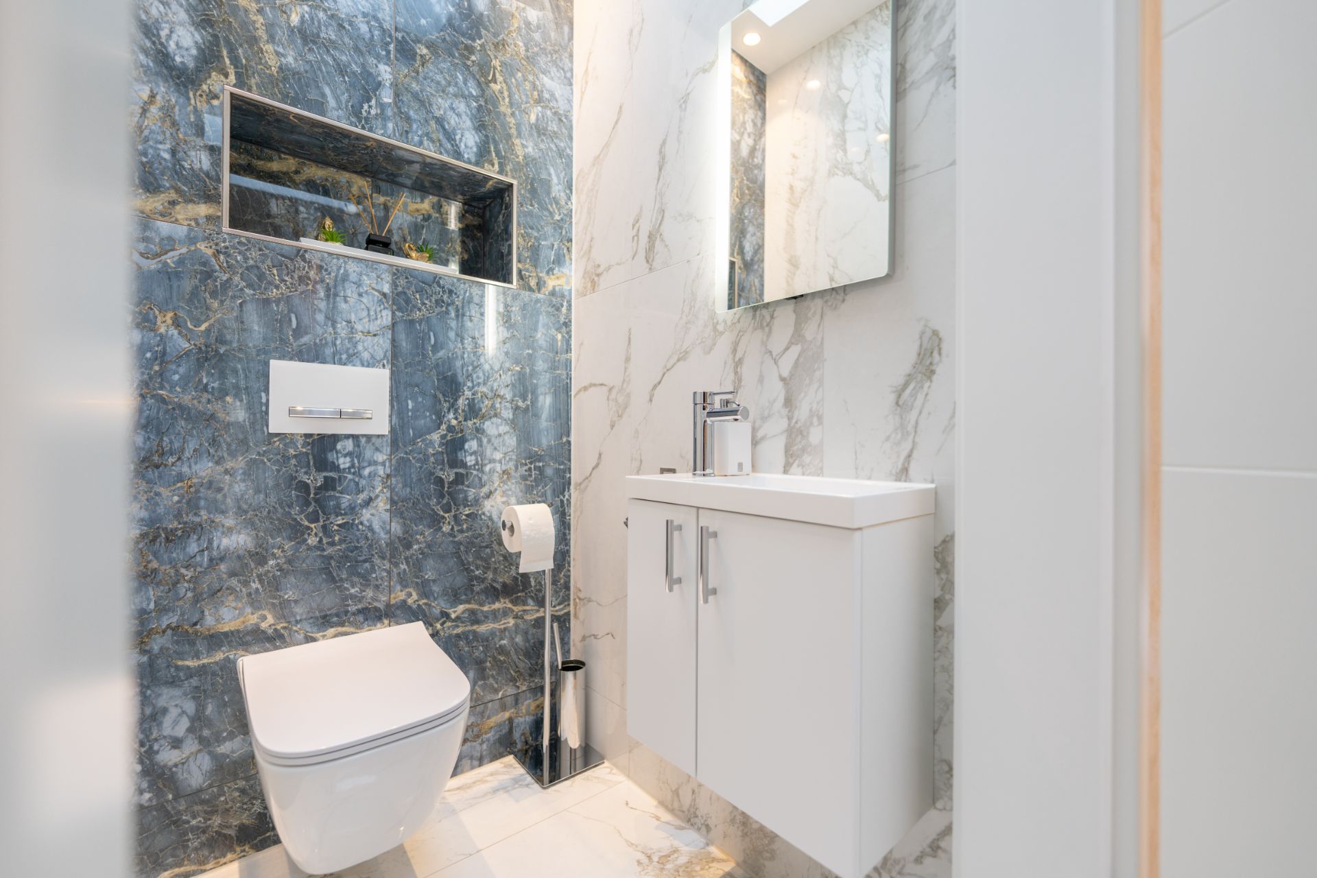 Modernes Badezimmer mit Wandtoilette, Marmorwänden und weißem Waschbeckenunterschrank.