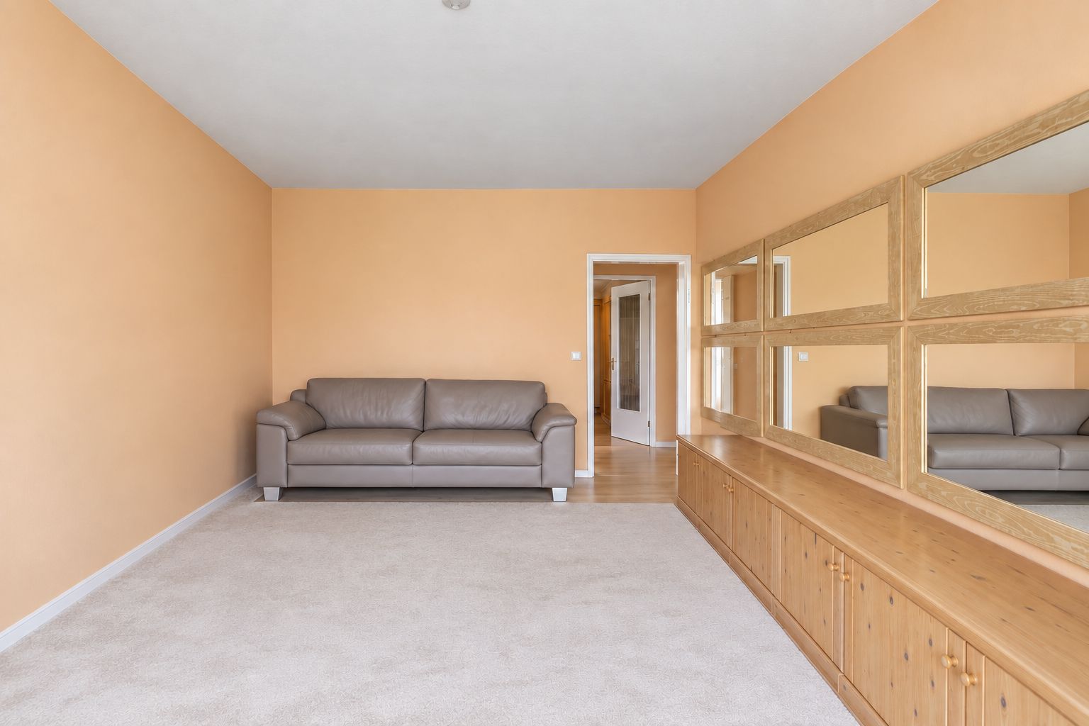 Helles Wohnzimmer mit beiger Couch, großem Spiegel und Holzkommode an orangefarbener Wand.