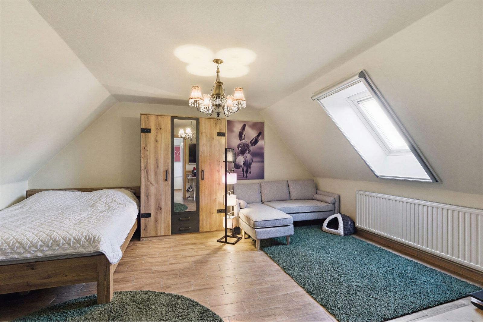 Helles Dachzimmer mit Bett, Kleiderschrank, Ecksofa, Teppichen und Dachfenster.