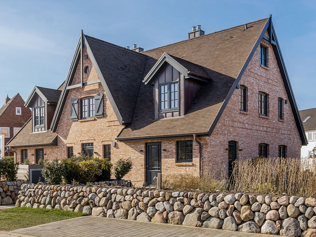 Backstein-Doppelhaus mit Satteldach und steinerner Gartenmauer im Vordergrund.