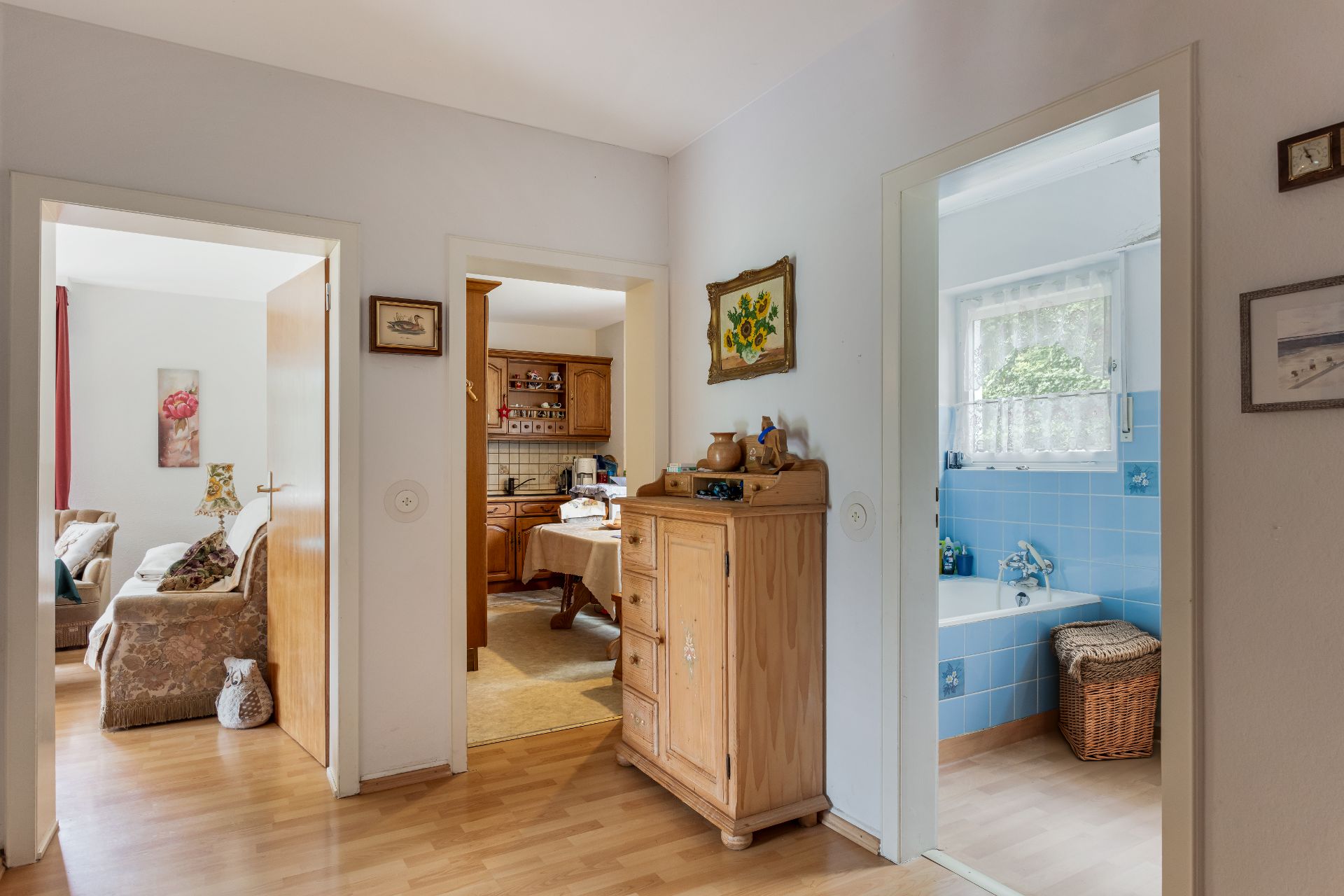 Flur mit Durchblick ins Wohnzimmer, Küche und ein Badezimmer mit blauen Fliesen.