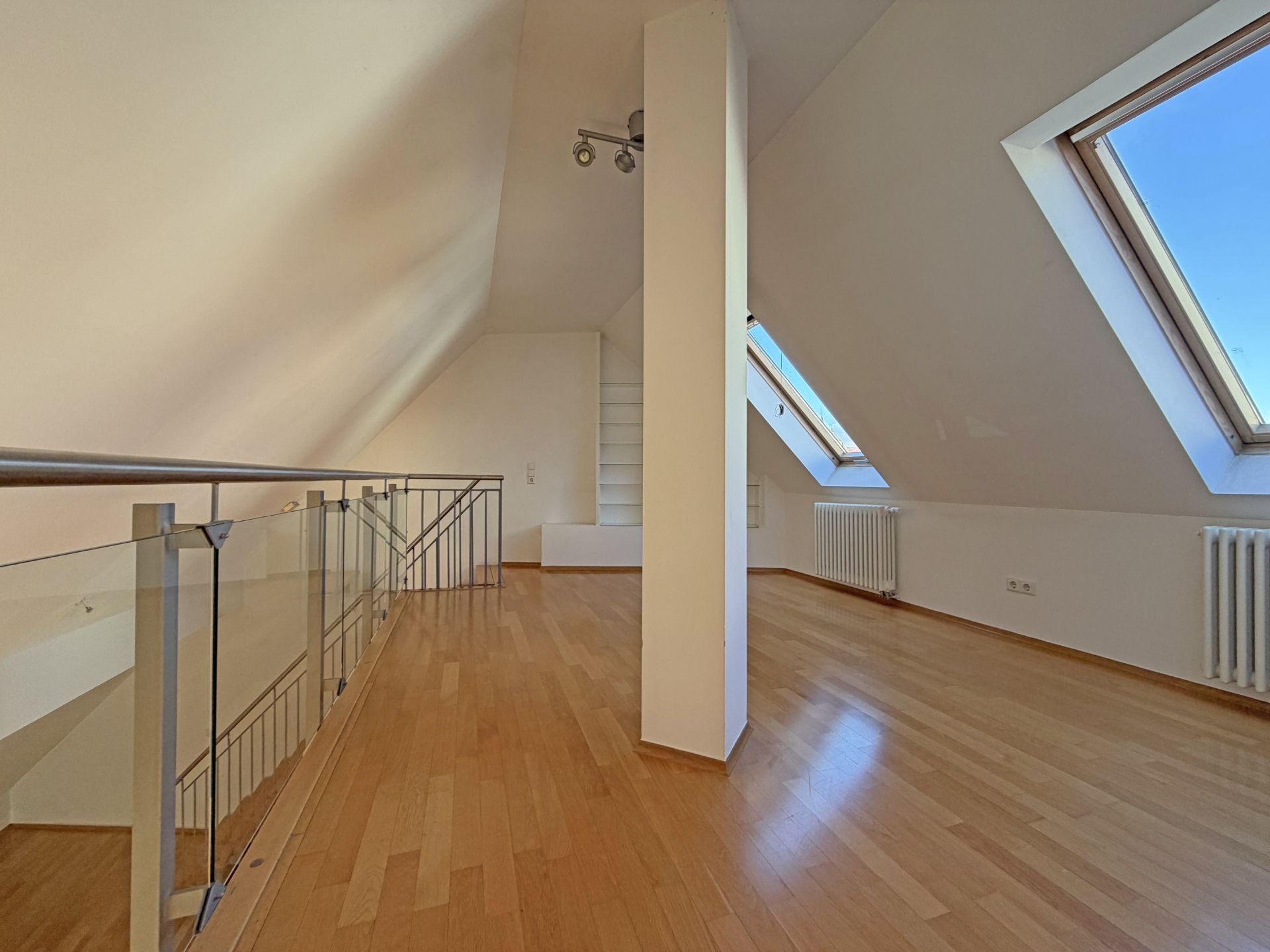 Helles Dachgeschosszimmer mit Holzfußboden, schrägen Decken und großen Dachfenstern.
