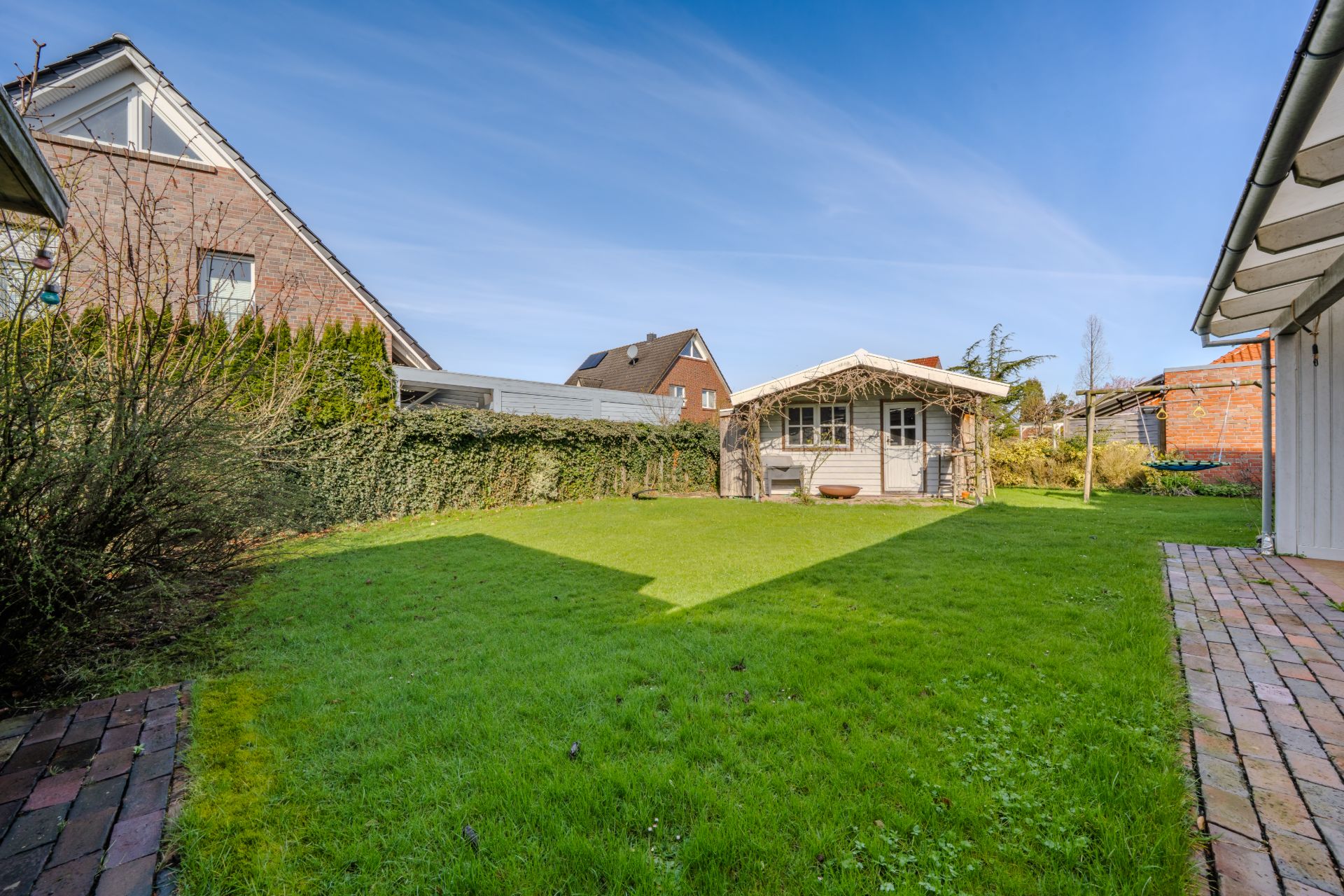 Garten mit grünem Rasen, Gartenhaus im Hintergrund und Ziegelwegen an den Seiten.