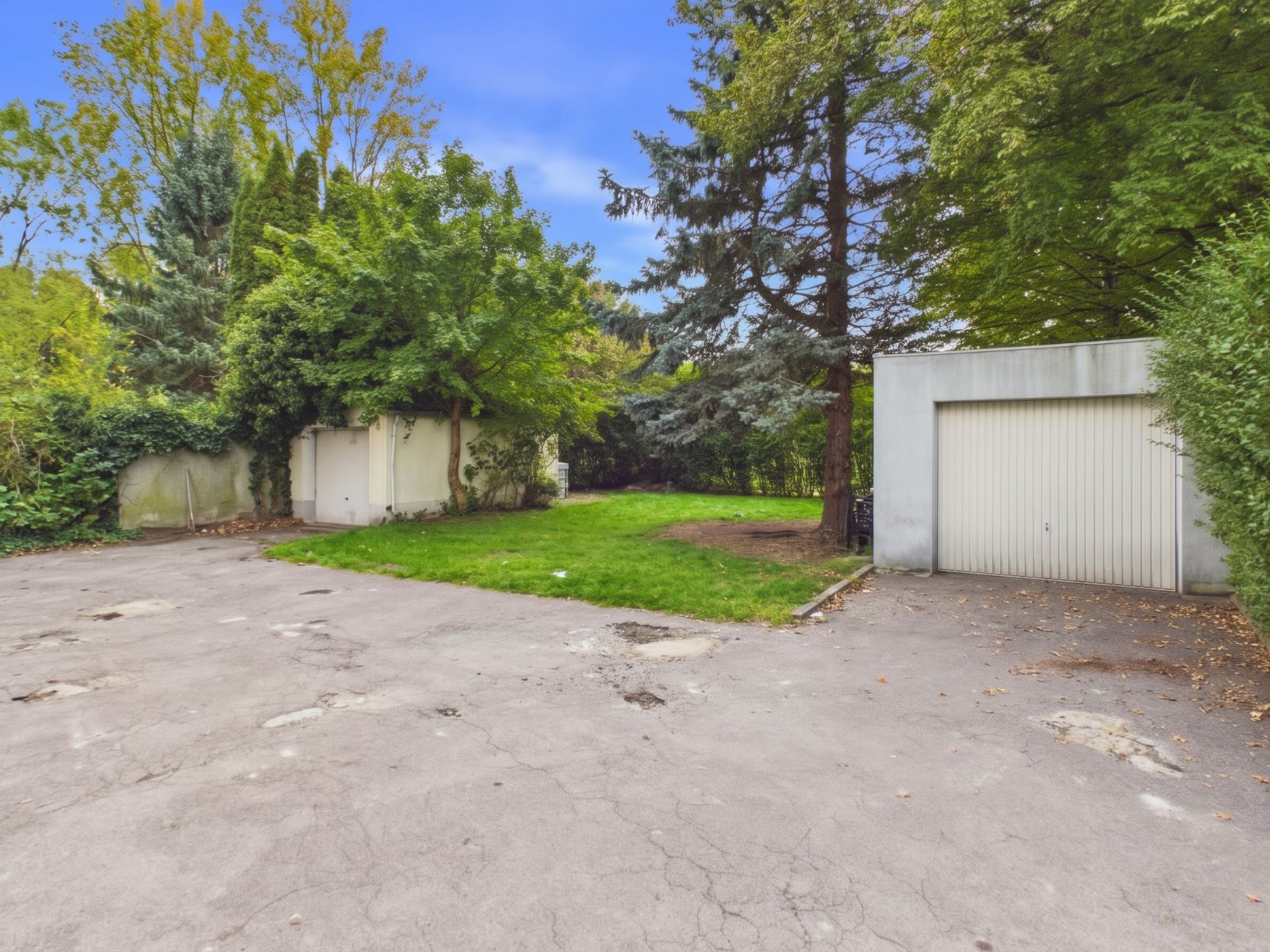 Hof mit Garage, Rasenfläche und Bäumen im Hintergrund.