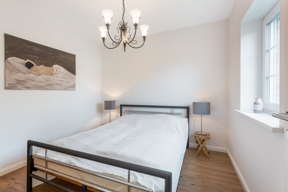 Helles Schlafzimmer mit Doppelbett, zwei Nachttischen mit Lampen und großem Fenster.