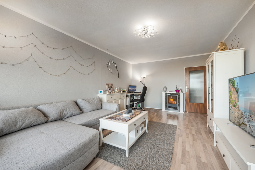 Wohnzimmer mit grauem Sofa, Couchtisch, Teppich, Schreibtisch, Kamin und Fernseher.
