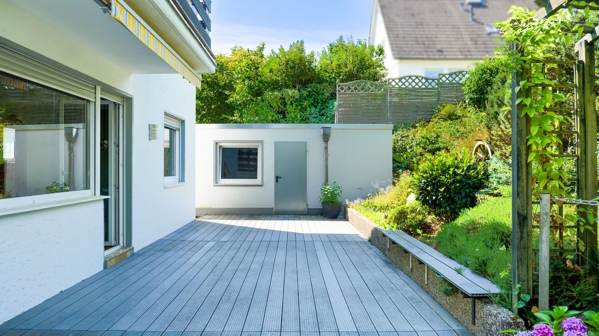Große Terrasse mit Holzdeck, angrenzendem Garten und modernem weißen Gebäudeteil.