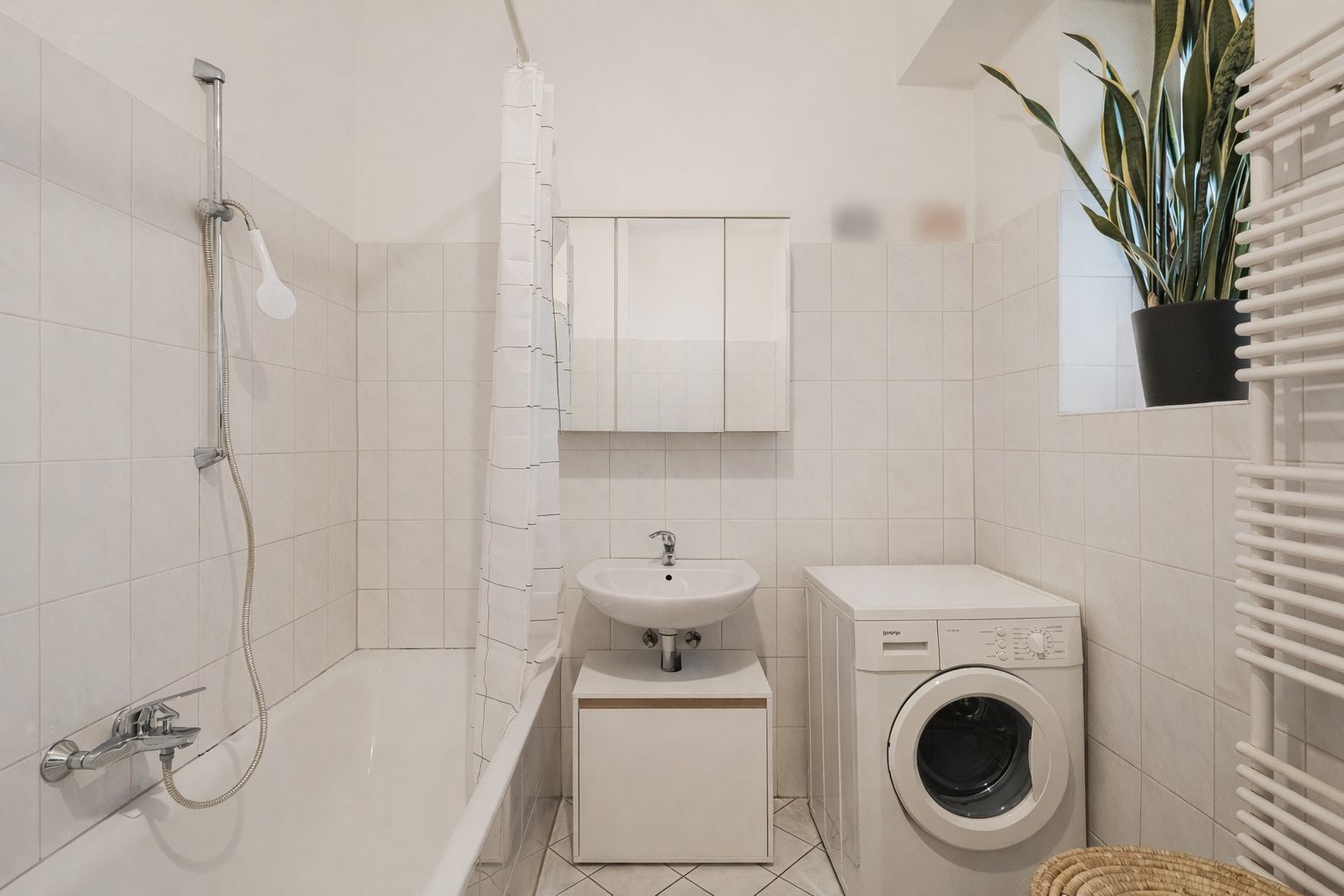 Helles Badezimmer mit Badewanne, Waschbecken, Waschmaschine und Pflanze auf dem Fensterbrett.