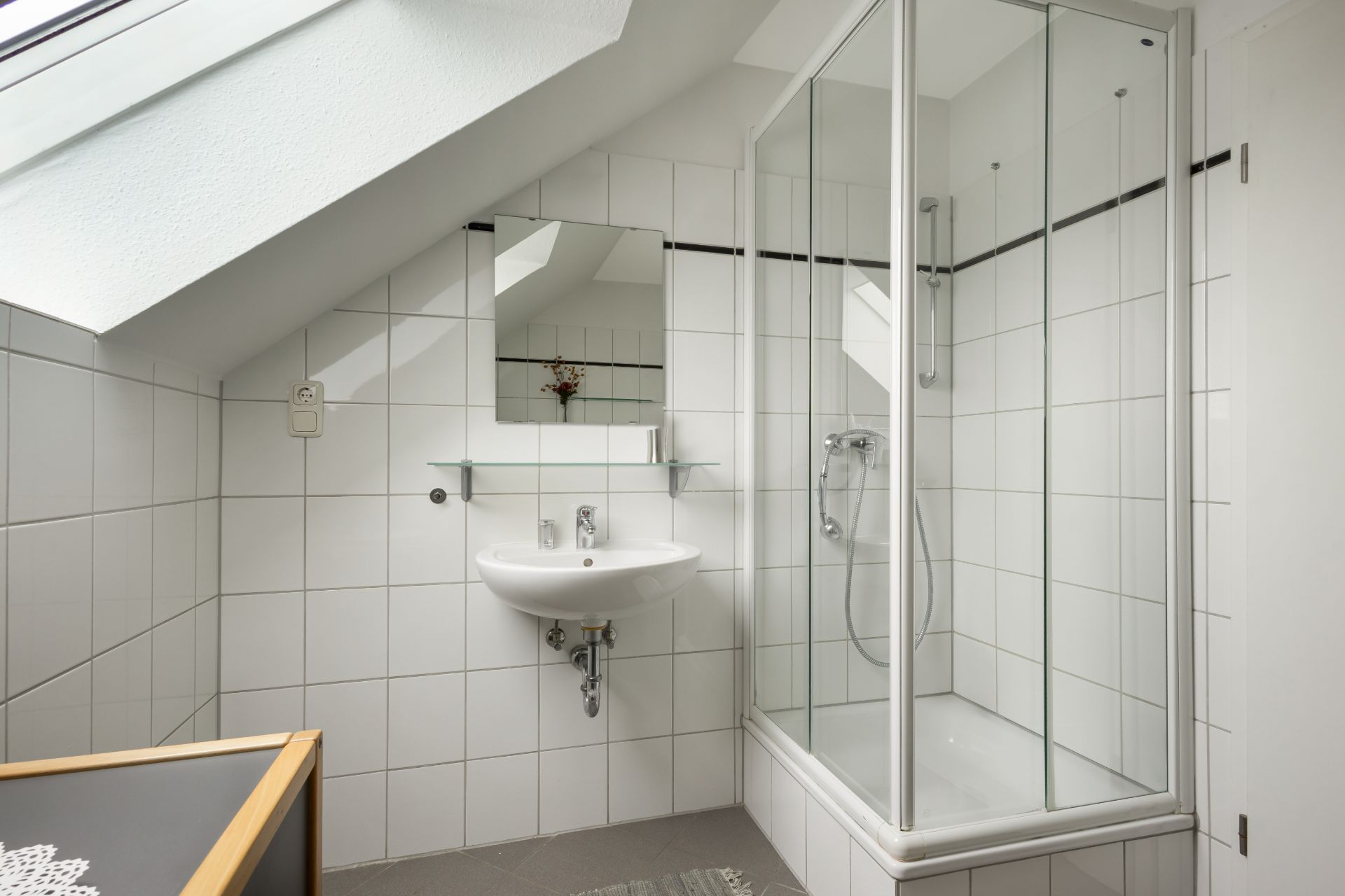 Helles Badezimmer mit Dachschräge, Dusche, Waschbecken und Spiegel.
