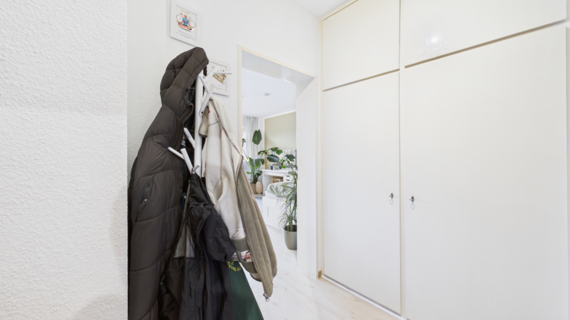 Flur mit Garderobe und mehreren Jacken, daneben ein großer weißer Einbauschrank.