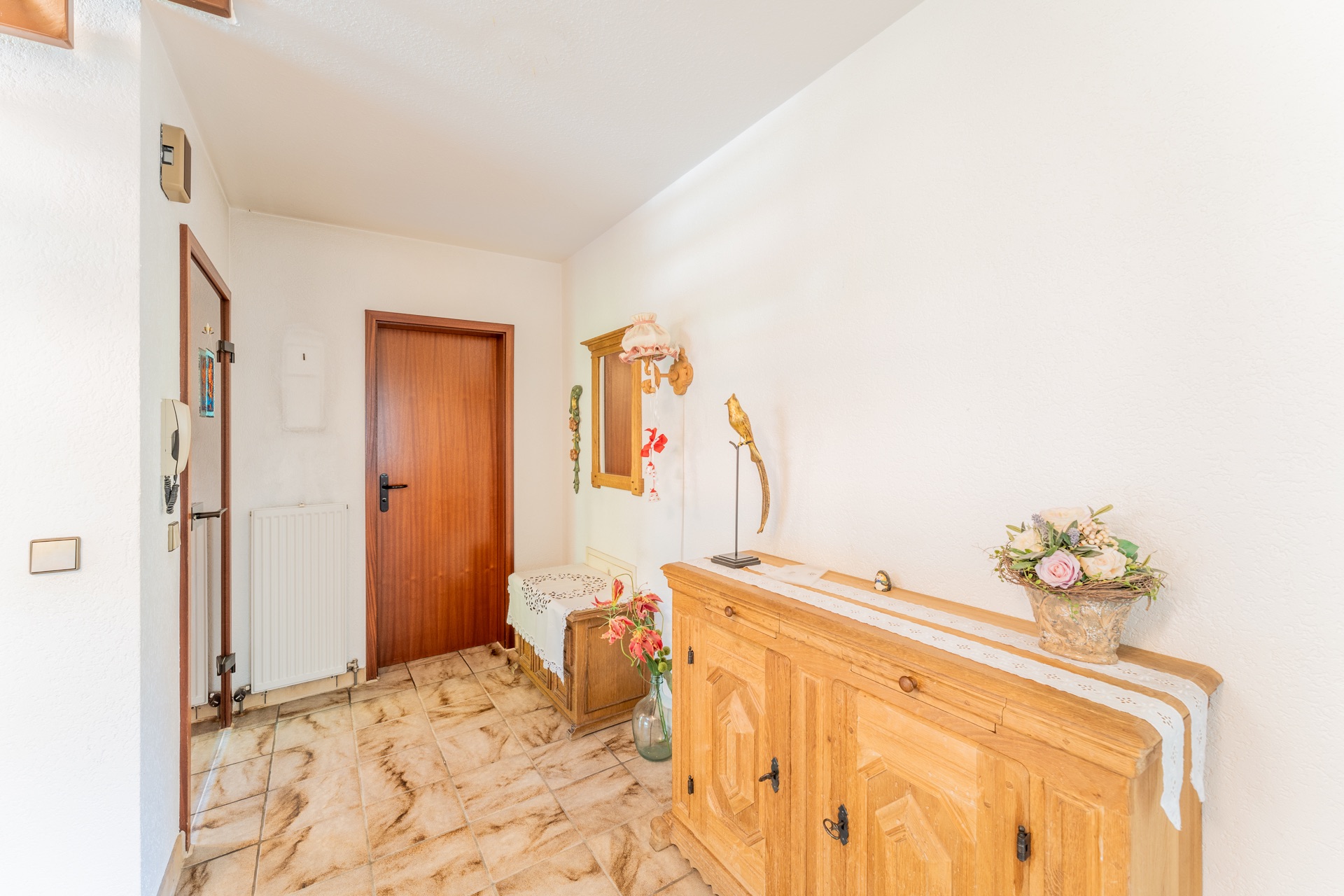 Heller Flur mit Holzmöbeln, Blumen und Dekorationen an den weißen Wänden.