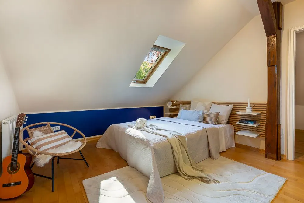 Schlafzimmer mit Doppelbett, Dachfenster, Sessel, Gitarre und Holzboden.