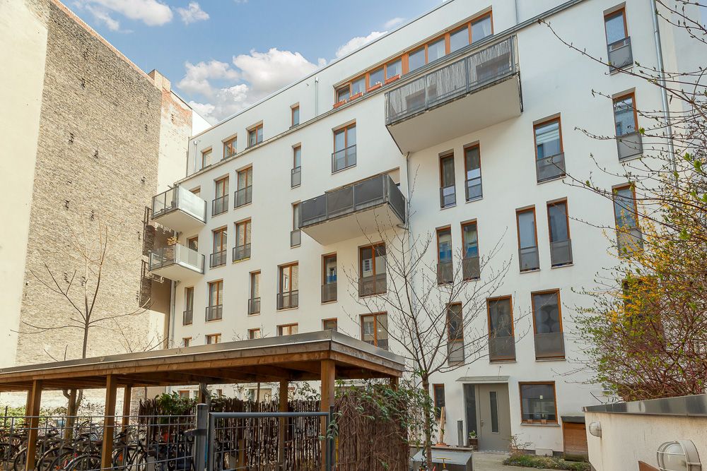 Mehrstöckiges Wohnhaus mit Balkonen und überdachtem Fahrradabstellplatz im Innenhof.