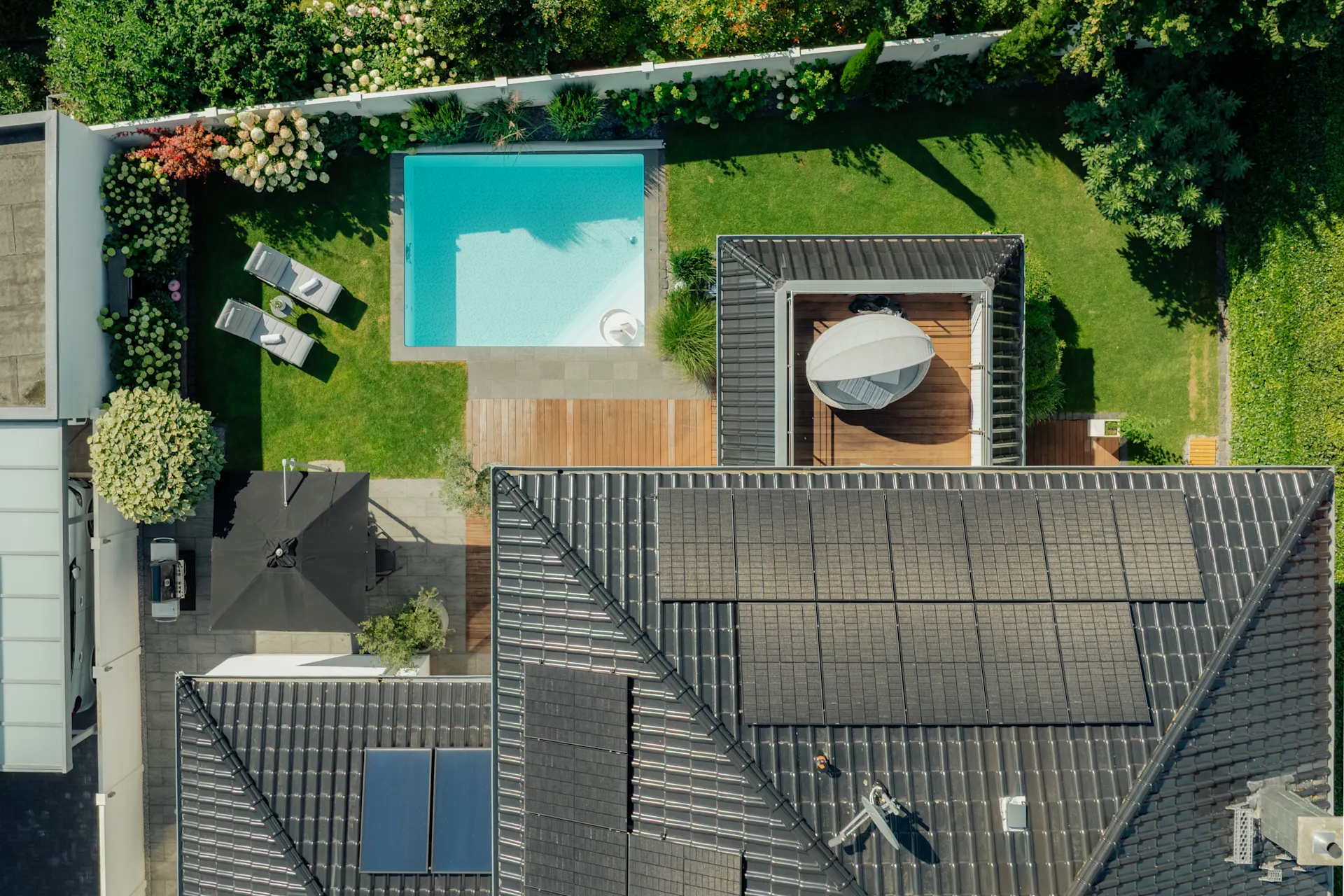 Luftaufnahme eines Gartens mit Pool, Liegestühlen, Terrasse und Hausdach mit Solarpanelen.