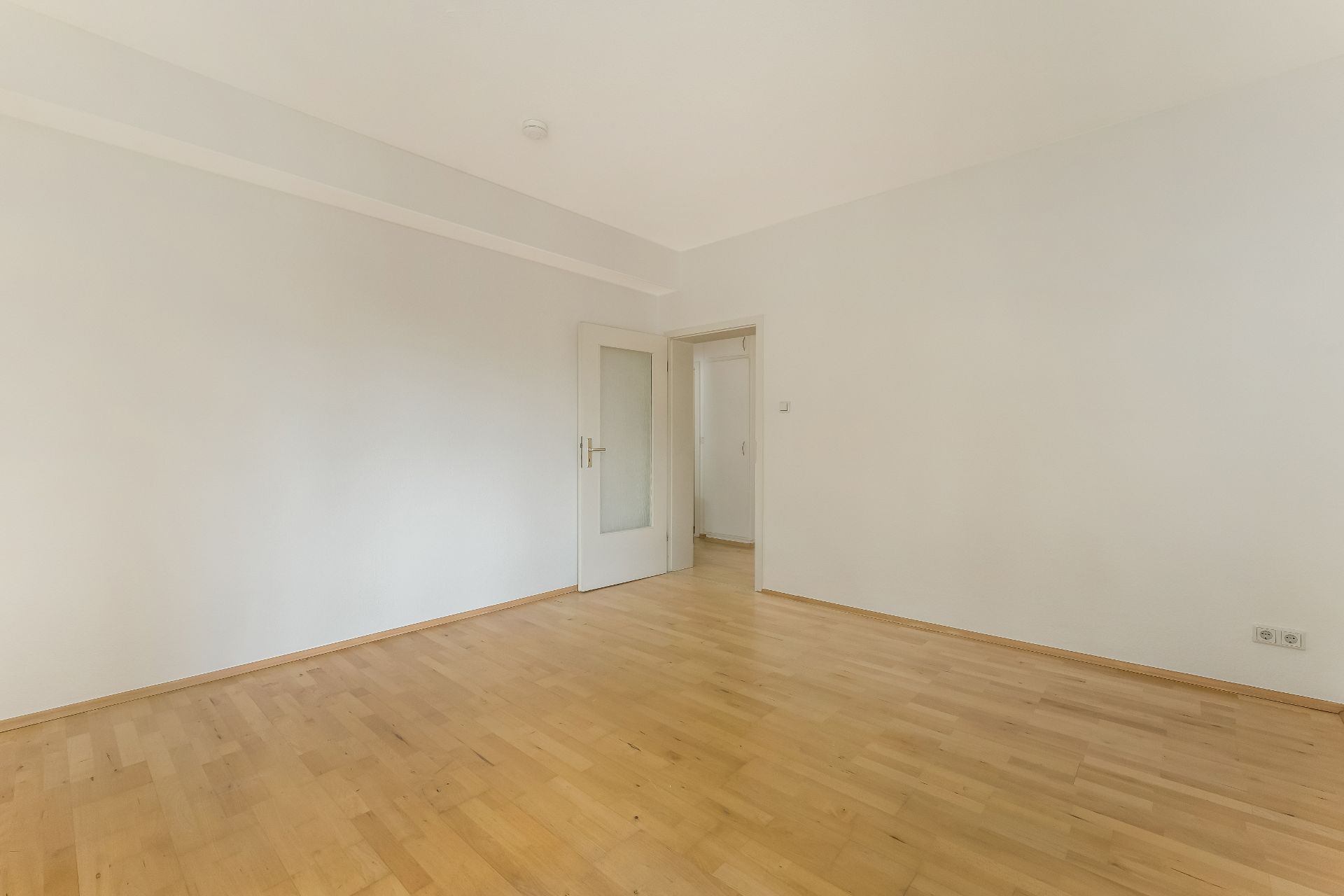Leerer Raum mit hellem Holzfußboden und weißer Tür, weiße Wände.