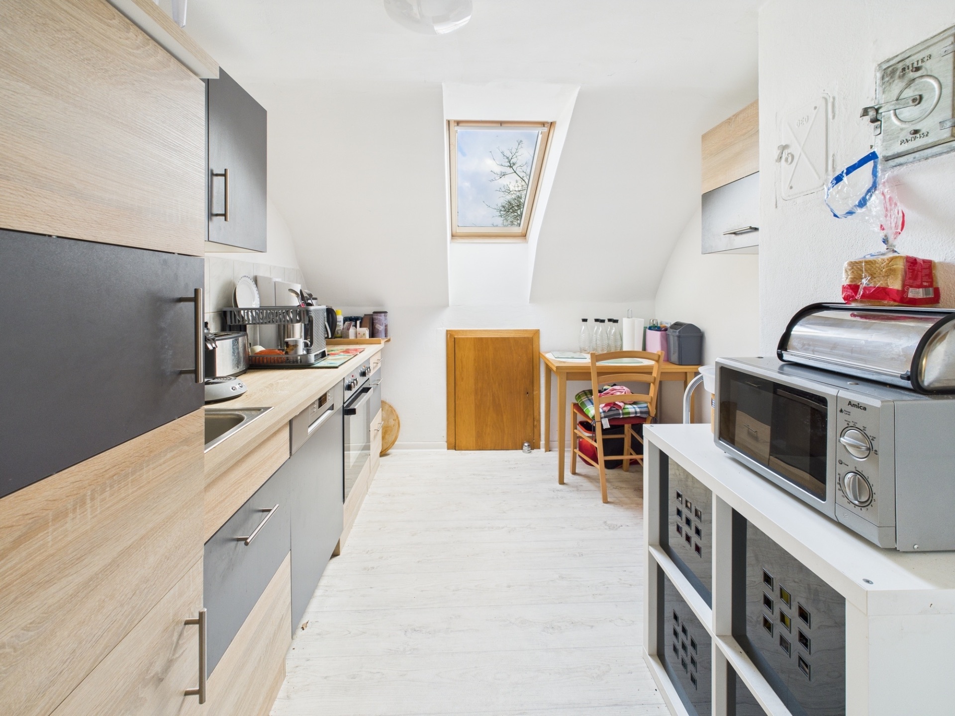 Helle Küche mit Dachfenster, Holzmöbeln, Mikrowelle und kleinem Esstisch mit zwei Stühlen.