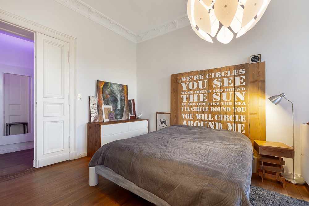 Schlafzimmer mit Doppelbett, Nachttischen, Kommode und Wandbild aus Holz mit Text.