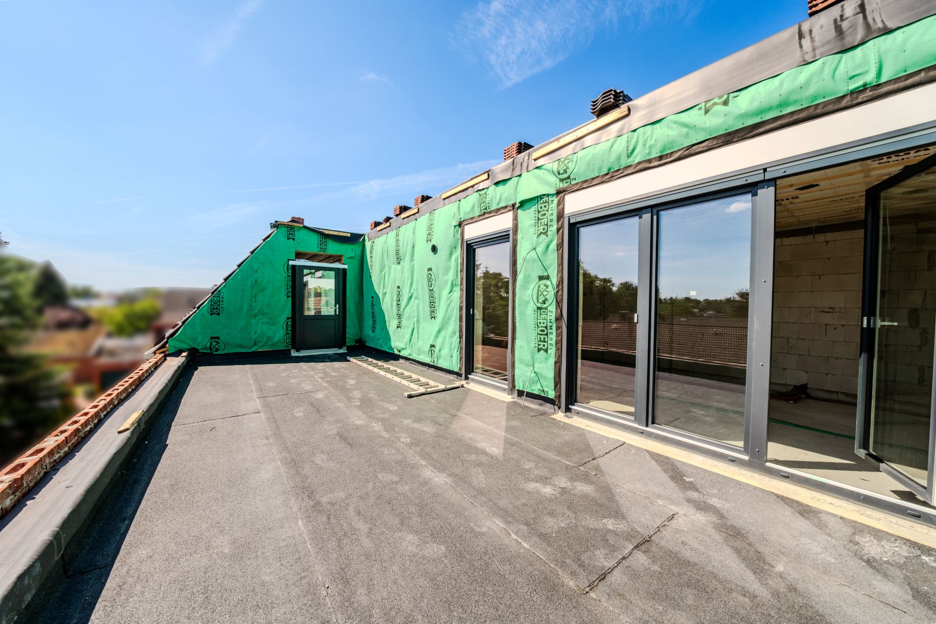Große Dachterrasse mit Schiebetüren und teilweise isolierter Wand, Gebäude im Rohbau.
