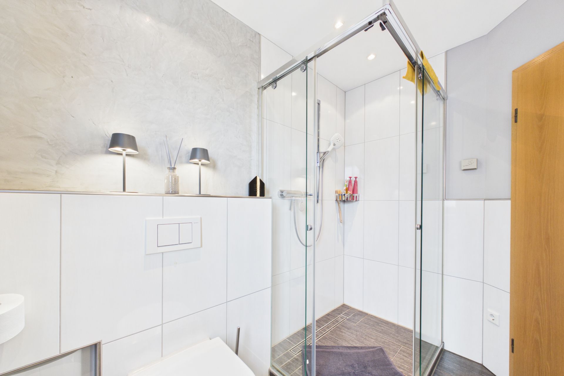 Modernes Badezimmer mit Glasdusche, weißen Fliesen und Wanddeko.