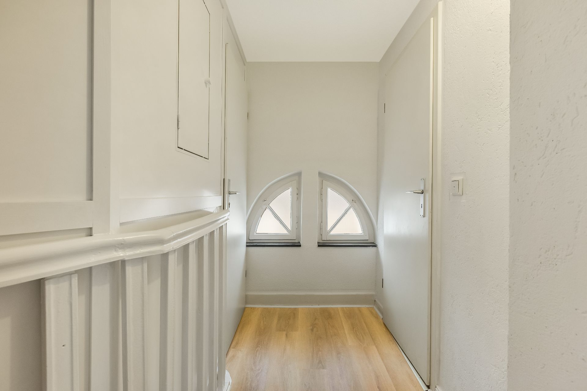 Heller Flur mit Holzfußboden und zwei halbkreisförmigen Fenstern am Ende.