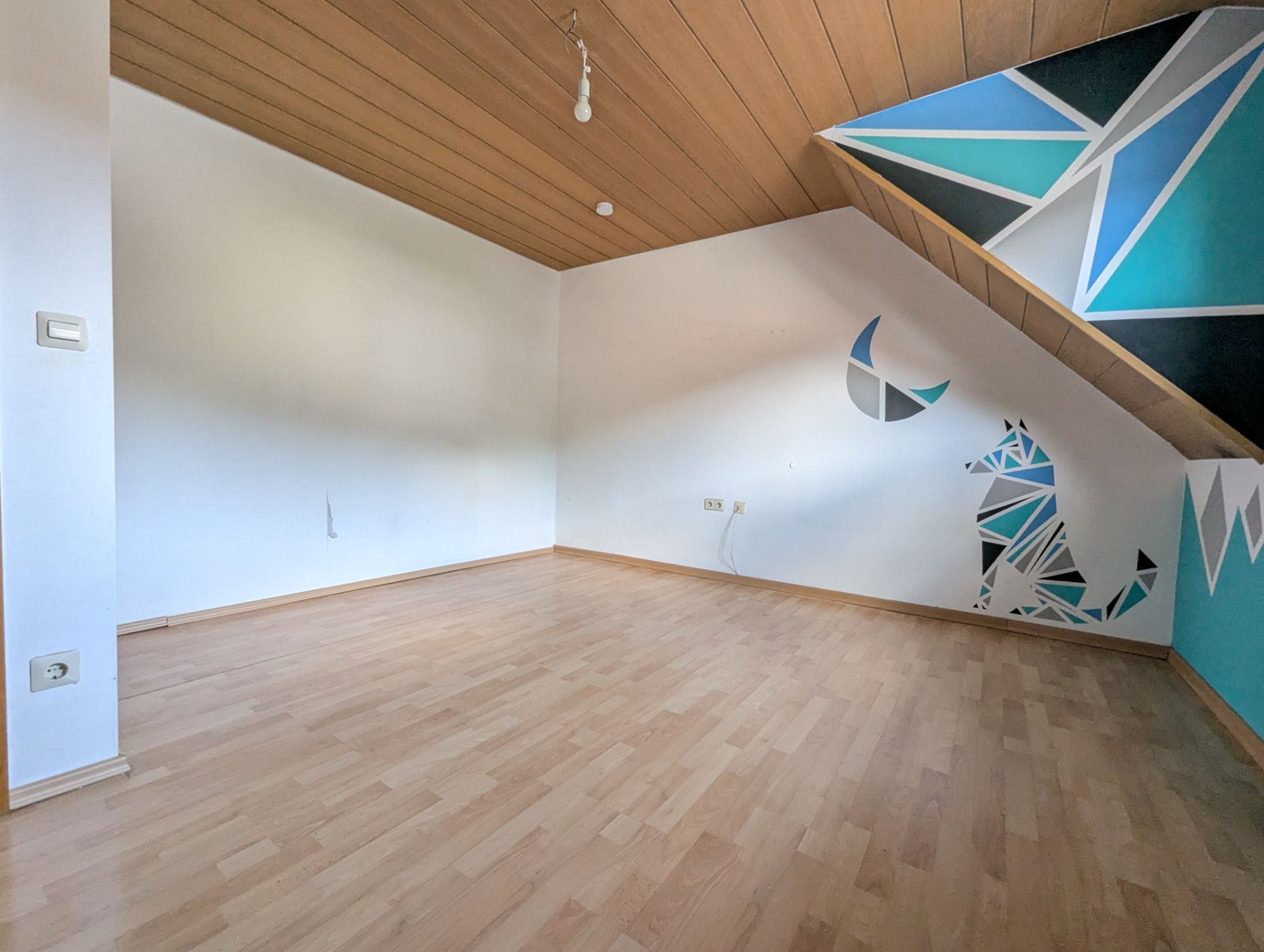 Leeres Zimmer mit Holzdecke, Laminatboden und geometrischer Wandmalerei eines Tiers und Mondes.