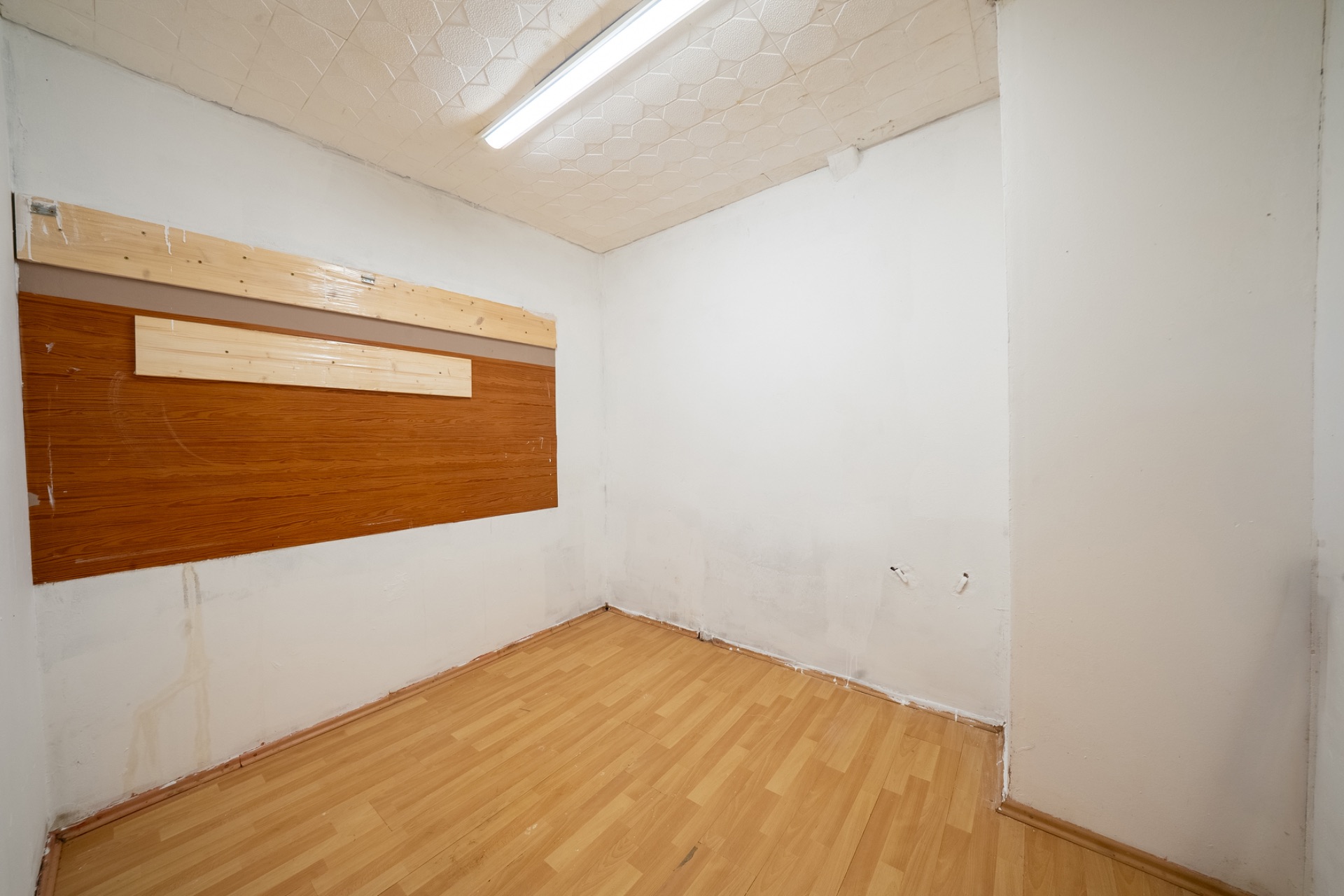 Kleiner Raum mit hellem Laminatboden, weißen Wänden und Holzpaneelen an einer Wand.