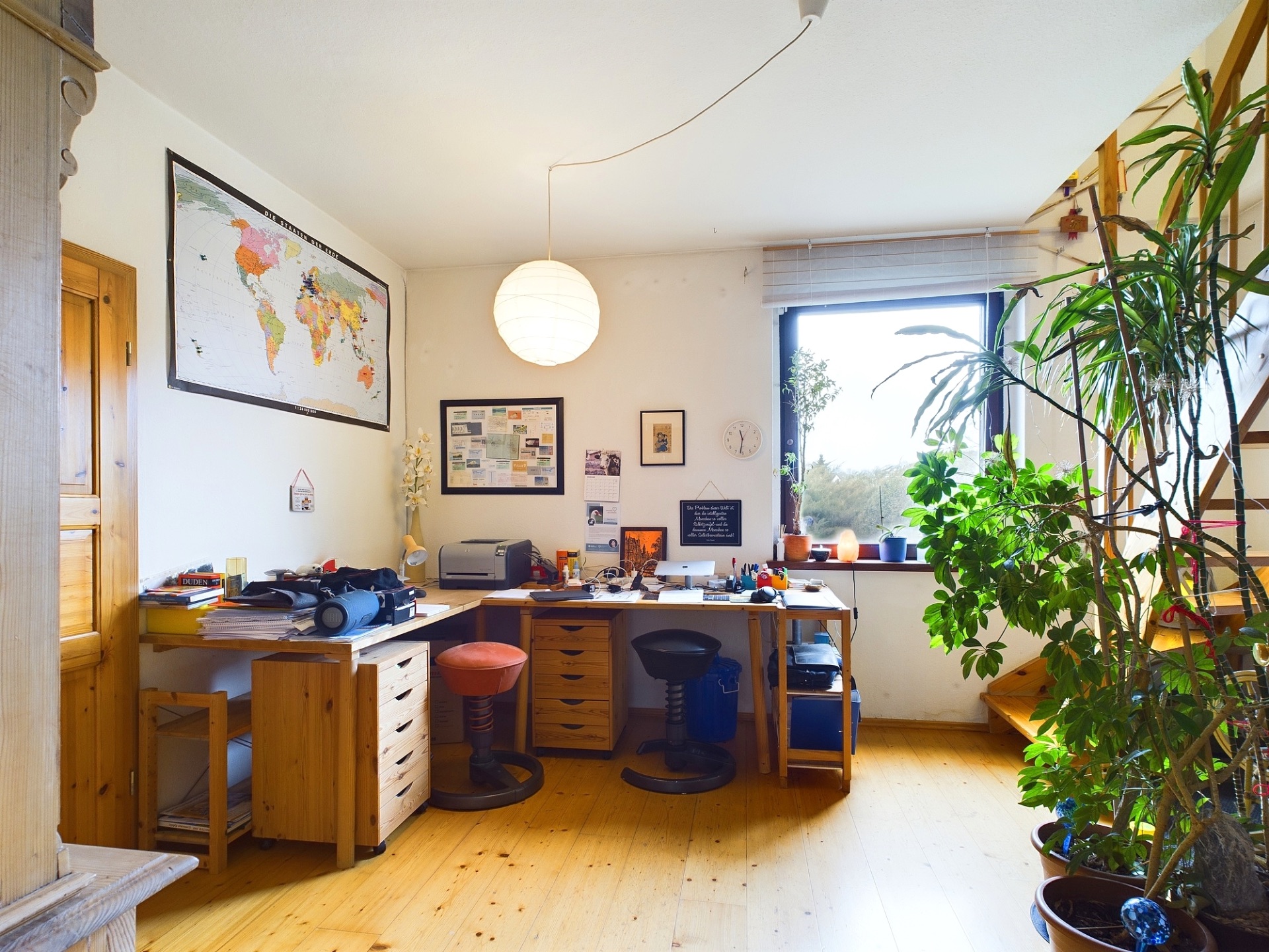 Helles Arbeitszimmer mit Holzmöbeln, zwei Stühlen, Pflanzen und großem Fenster.