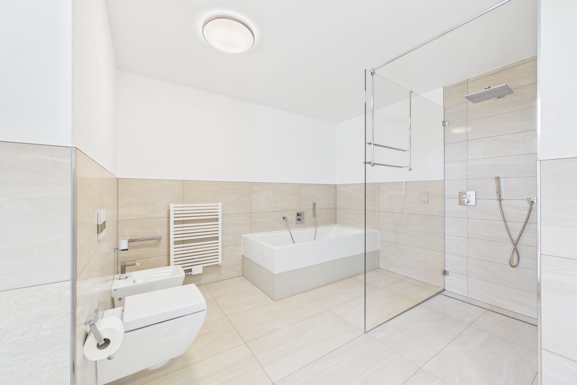 Modernes, helles Badezimmer mit Badewanne, Dusche, WC, Bidet und Handtuchheizkörper.