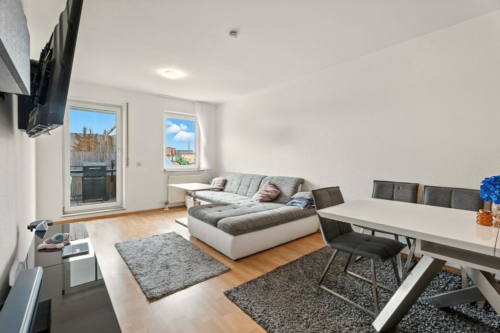 Helles Wohnzimmer mit Ecksofa, Esstisch, Teppichen und Zugang zum Balkon.