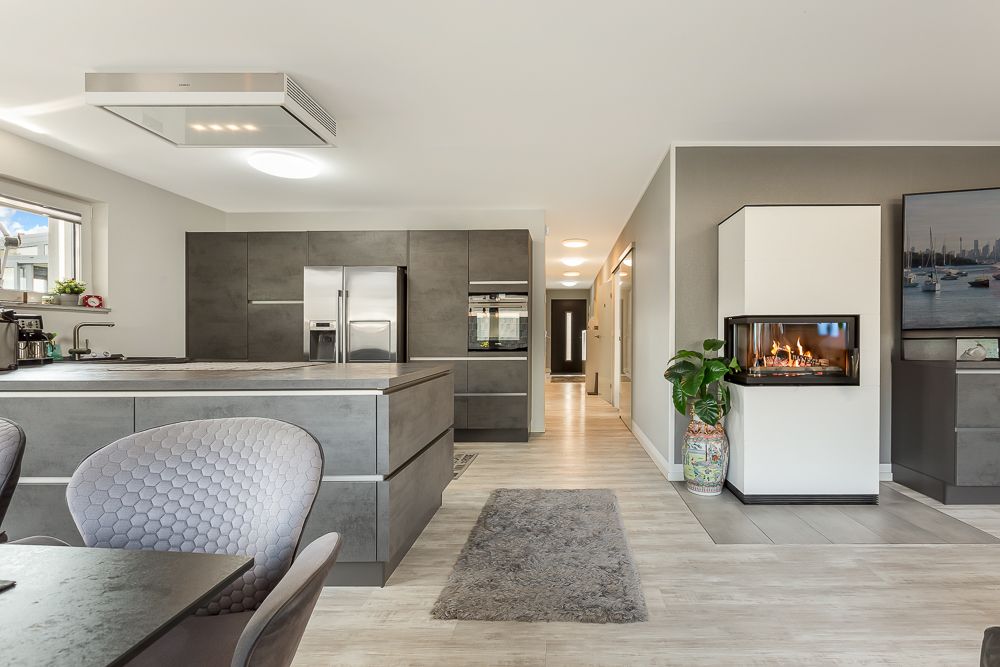 Moderne Küche mit Kücheninsel, Essbereich, Kamin und hellen Fußboden im offenen Wohnraum.