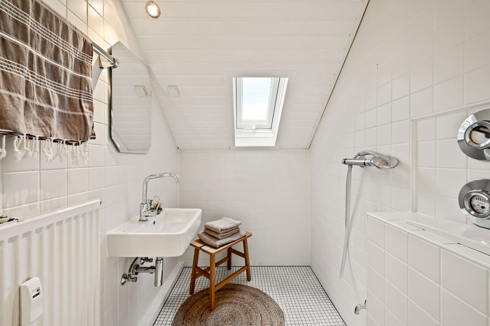 Helles Badezimmer mit Waschbecken, Spiegel, Dusche, Handtuch und Fenster im Dach.