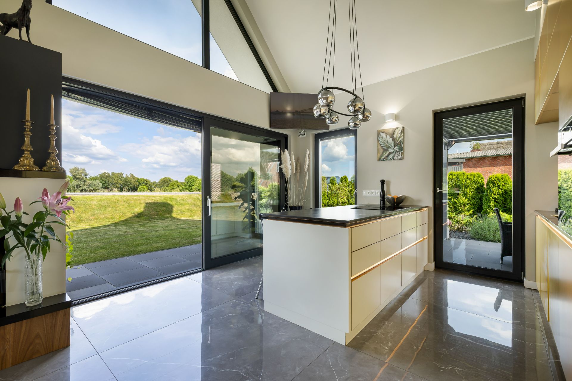 Moderne helle Küche mit Kochinsel und großen Glas-Schiebetüren zum Garten.