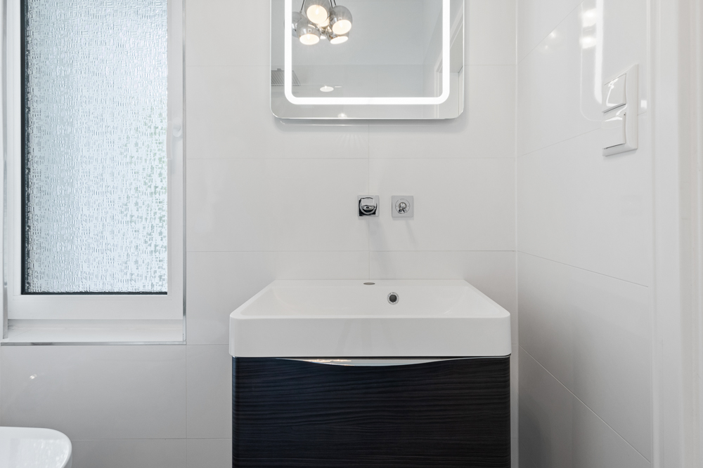Modernes Badezimmer mit Waschbecken, beleuchtetem Spiegel und Fenster mit Milchglas.