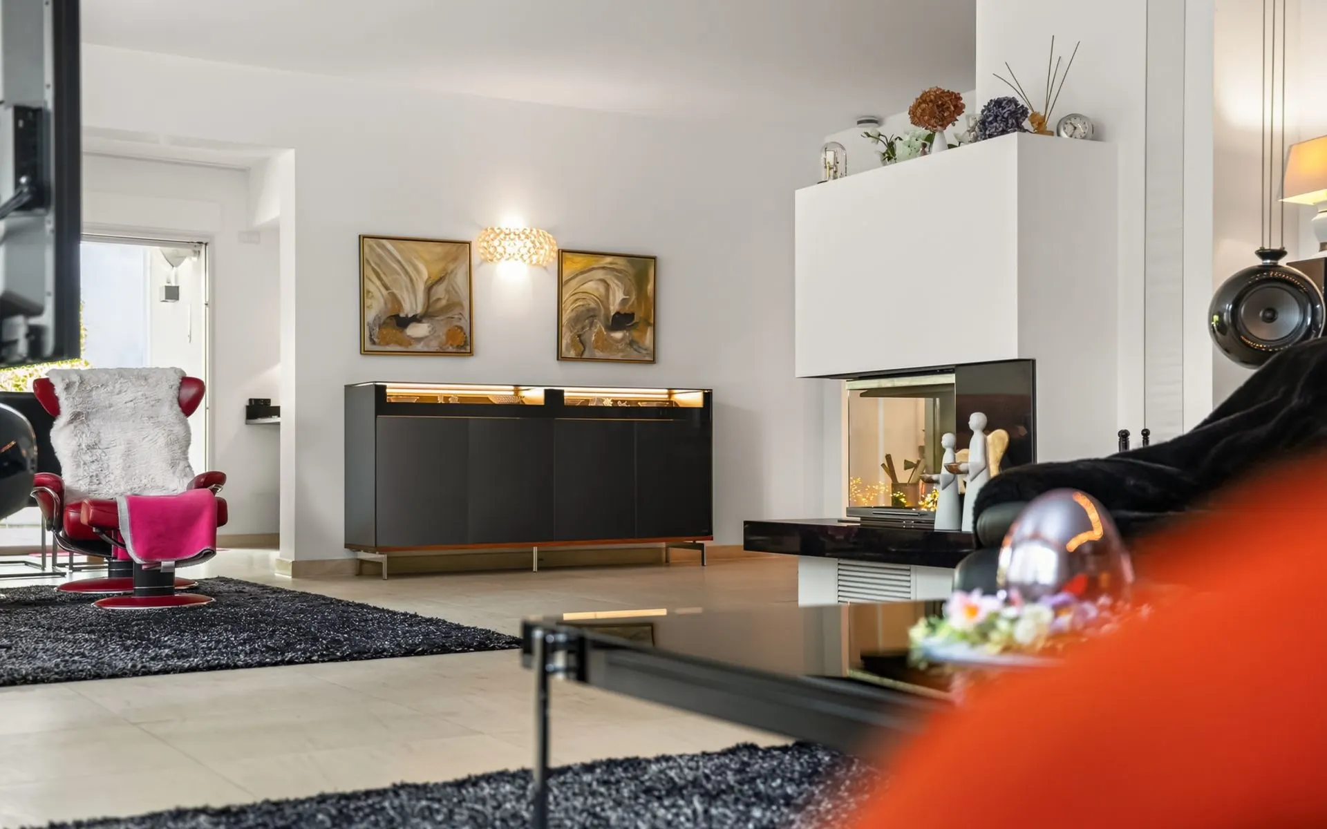 Modernes Wohnzimmer mit schwarzem Teppich, Kamin, Kunst an der Wand und einem roten Sessel.