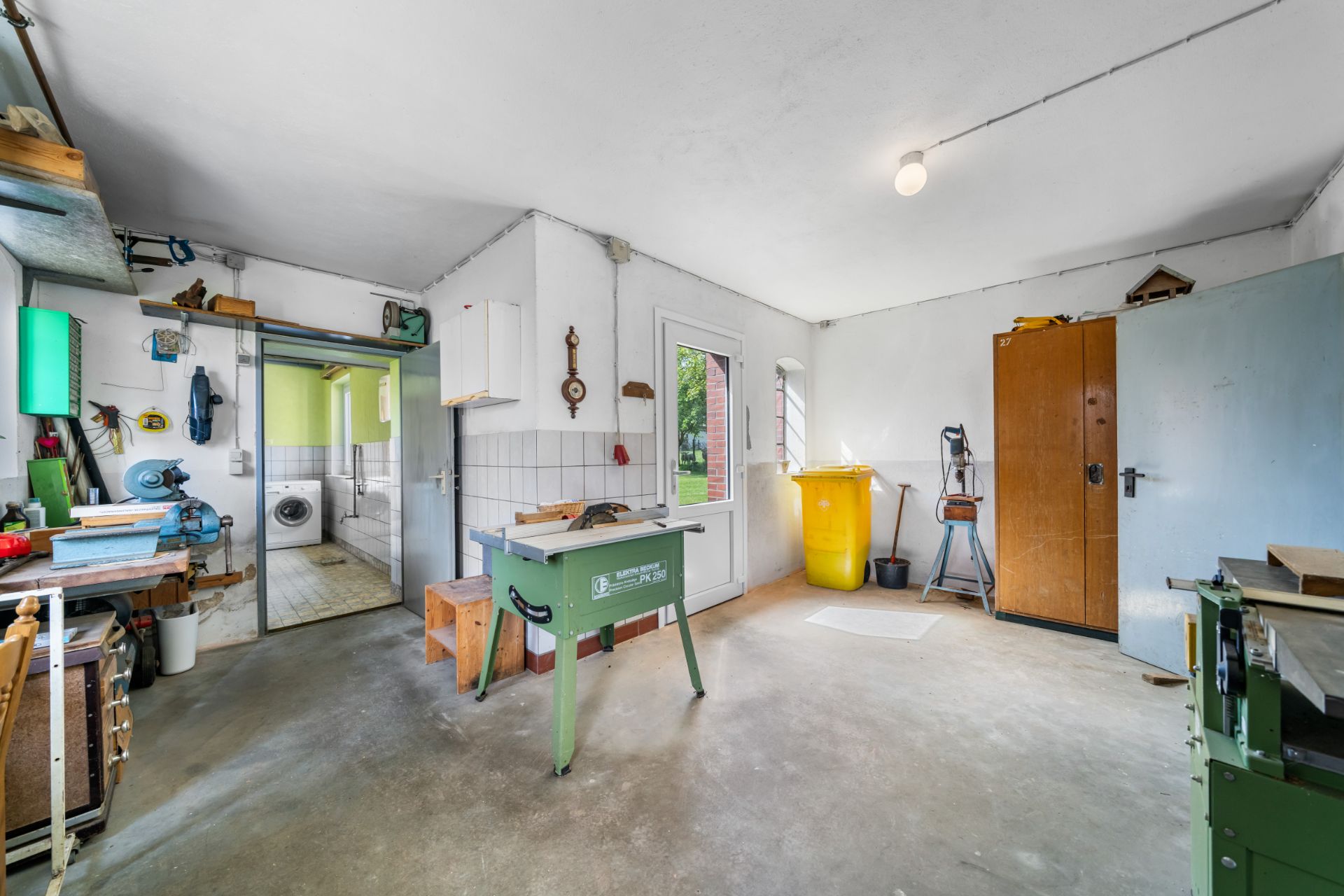 Geräumige Werkstatt mit Werkbänken, Werkzeugen, Schränken und einer Tür zum Garten.