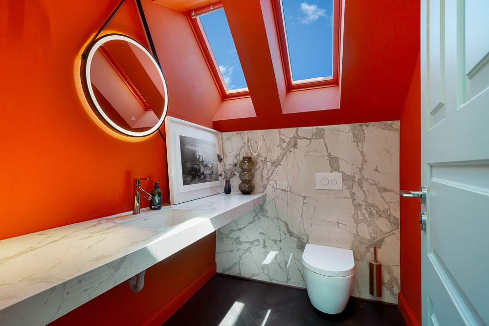 Modernes Bad mit roter Wand, Dachfenstern, rundem Spiegel und WC auf Marmorrückwand.