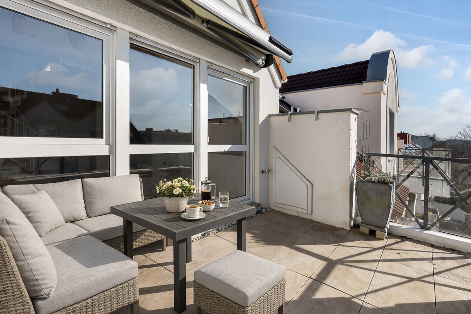 Moderne Dachterrasse mit Sitzgruppe, Tisch und Blumendekoration bei Tageslicht.