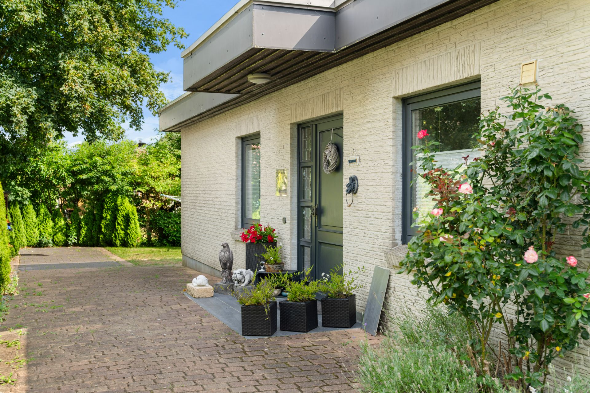 Eingangsbereich eines Hauses mit Blumen, Topfpflanzen und Steinfiguren neben der Haustür.