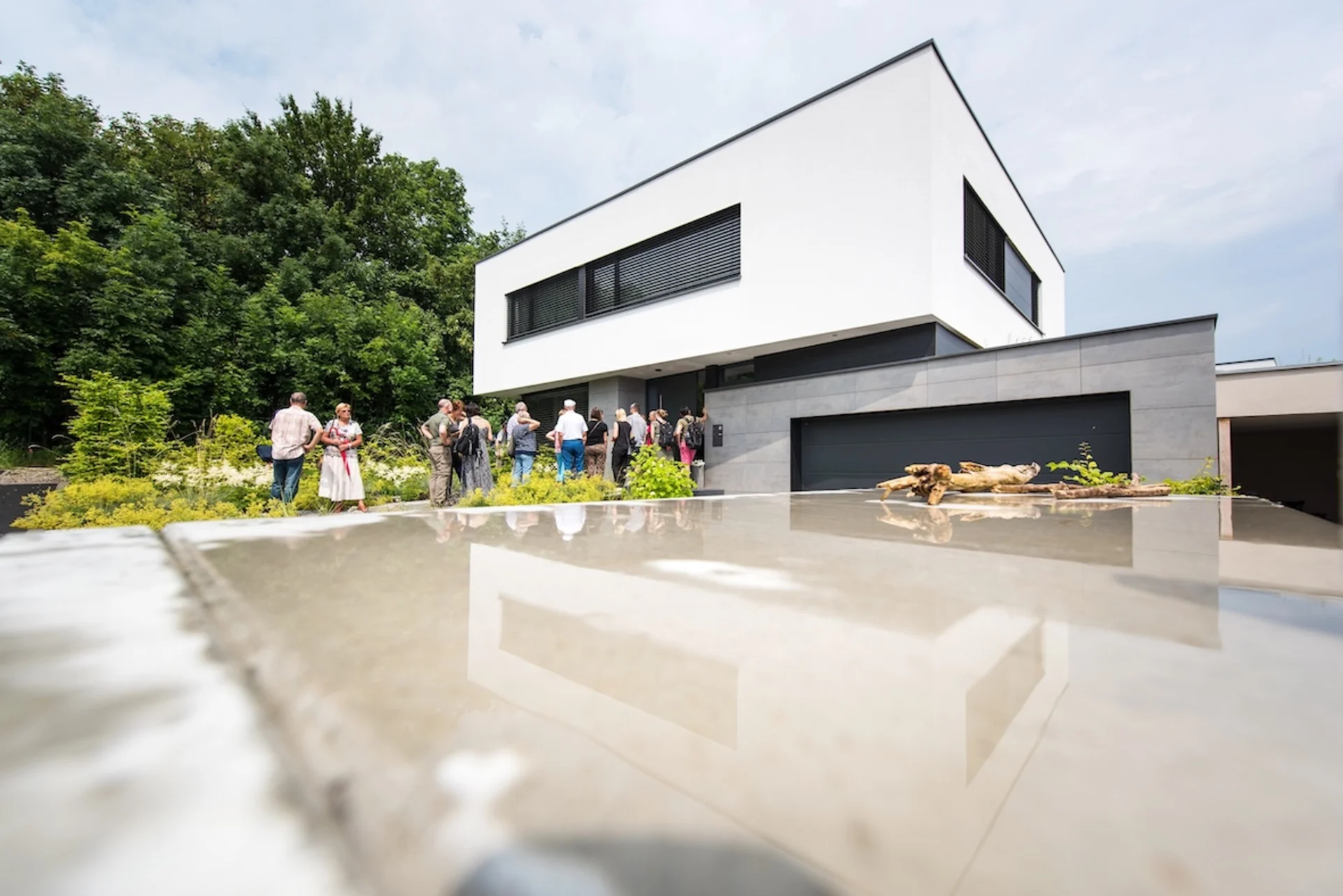 Mehrere Personen stehen vor einem modernen, weißen Wohnhaus mit flachem Dach und großem Garagentor.